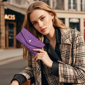 Primer plano de una cartera de mano morada con grabado de cocodrilo sostenida por una modelo.