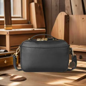 Vintage black leather camera bag with gold hardware in a rustic workshop setting