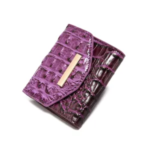 Vista detallada de una cartera morada con diseño de cocodrilo y adorno dorado.