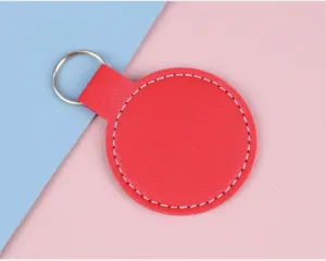 Vue détaillée d'un porte-clés rond en cuir rouge avec coutures blanches sur fond pastel