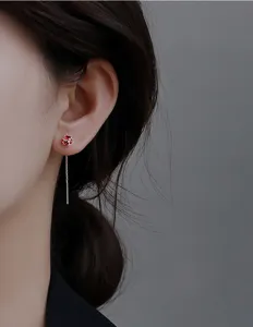 Nahaufnahme eines eleganten Ohrrings mit rotem Zirkonia und feiner Kette an einem Modell.