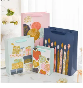 Collection of festive birthday gift bags featuring gold glitter patterns and silk ribbon handles.