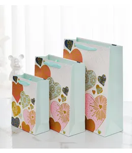 Mint green gift bags with gold glitter heart patterns in three sizes for parties