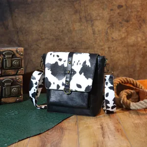 Retro Western crossbody bag with cow print flap and strap shown in a vintage setting