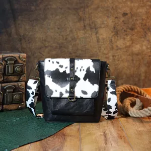 Vintage western style crossbody bag featuring a cow print flap and brass hardware.