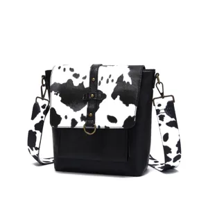 Retro western style crossbody bag featuring black and white cow print flap and wide strap.