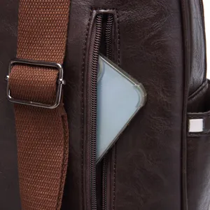 Close-up of the vertical zipper pocket on a dark brown textured leather backpack.