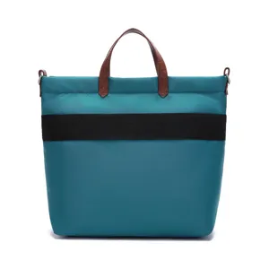 Close-up of a teal waterproof canvas tote bag with brown leather handles and black band.