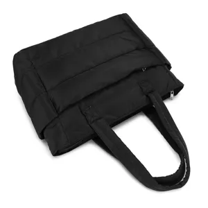 High-angle detail view of a black quilted padded travel tote bag with top zipper