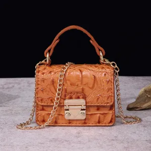 Detalle del bolso marrón con textura de cocodrilo, cierre dorado y correa de cadena.