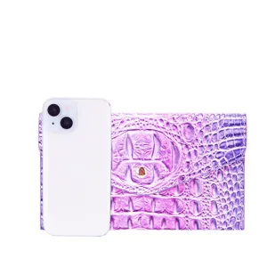 Cartera de mano violeta con patrón de cocodrilo junto a un móvil para referencia.