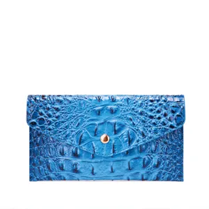 Detalle de cartera de mano en cuero azul con textura de cocodrilo y botón dorado