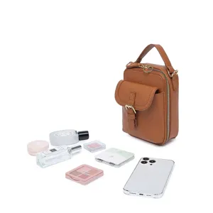 Bolso bandolera de piel granulada marrón mostrado con diversos cosméticos y un móvil