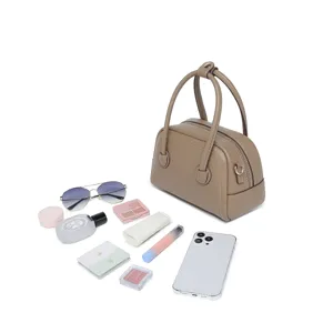Mini bolso Boston de cuero caqui mostrado con artículos diarios para escala