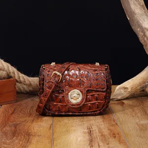 Detalle de un bolso bandolera vintage de cuero marrón con grabado de cocodrilo sobre madera
