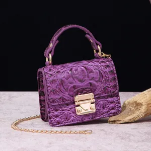 Primer plano de bolso de lujo en cuero violeta con grabado de cocodrilo y cierre dorado.