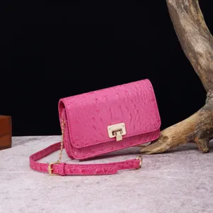 Detalle de un bolso bandolera rosa con grabado de cocodrilo y cierre metálico en dorado.