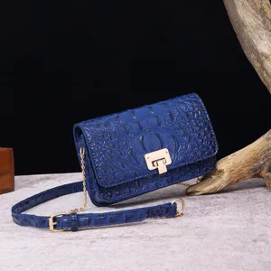 Detalle de un bolso de hombro azul con relieve de cocodrilo y herrajes dorados