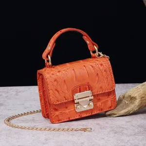 Detalle de mini bolso vintage naranja con patrón de cocodrilo y cadena dorada.
