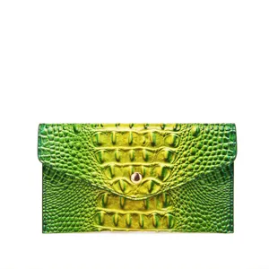 Detalle de una cartera de mano con grabado de cocodrilo y degradado verde y amarillo.
