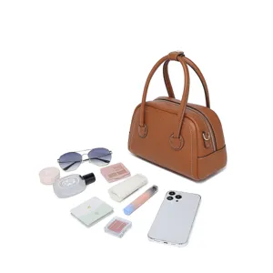 Mini bolso Boston de cuero marrón con elementos esenciales diarios como referencia