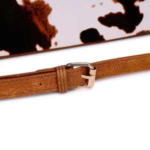 Primer plano de la correa de ante marrón y hebilla dorada del bolso con manchas.