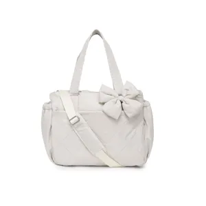 Dettaglio di una borsa a tracolla trapuntata beige con un grande fiocco decorato.