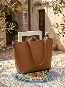 Bolso tote grande de cuero marrón con un libro y una botella en un jardín soloado