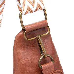 Detalle de hebilla de bronce y correa ancha bordada en bolso de cuero PU marrón