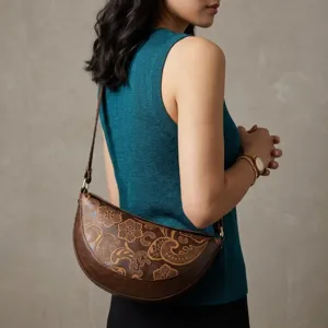Detalle del patrón floral grabado en un bolso de hombro marrón con forma de media luna.