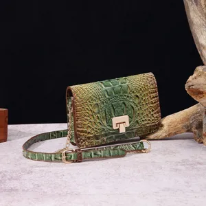 Primer plano de bolso bandolera verde con relieve de cocodrilo y cierre a presión dorado