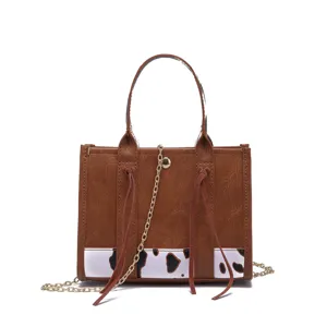 Detailed view of brown faux leather mini tote bag featuring cow print and gold chain strap