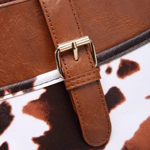 Detail shot of the golden pin buckle and textured cow print leather on a western bag.