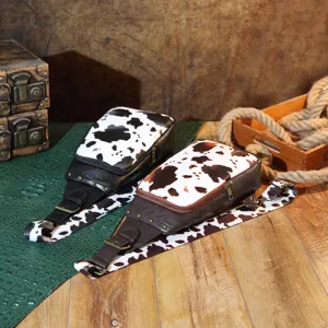 Vintage western cow print sling bags with metal rivets on a rustic wooden table
