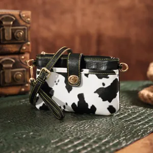 Close-up of a vintage cow print crossbody bag with golden clasp on textured green mat