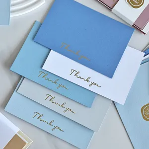 Dettaglio della scritta dorata 'Thank you' su biglietti di auguri minimalisti blu e bianchi