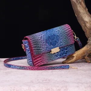 Detalle de un vibrante bolso bandolera de cuero con relieve de cocodrilo en lila y azul.