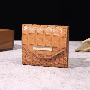 Detalle de una cartera de mujer marrón de tres pliegues con textura de cocodrilo.