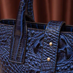 Primer plano de bolso de mano azul oscuro en relieve de cocodrilo con tachuelas.