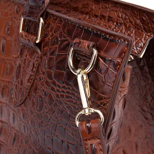 Primer plano de herrajes dorados y textura de cocodrilo en bolso vintage marrón.