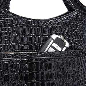Detalle de bolso negro brillante con grabado de cocodrilo y bolsillo trasero funcional