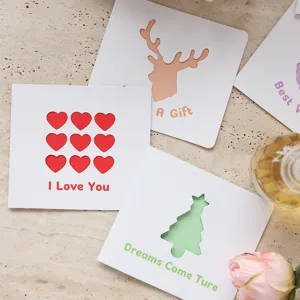 Primo piano di biglietti d'auguri quadrati traforati con I Love You e motivi festivi.