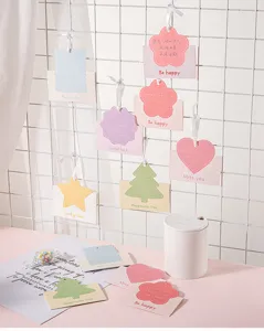 Detail von bunten Mini-Grußkarten mit Bändern an einer weißen Gitterwand.