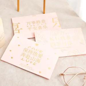 Gros plan de cartes de vœux roses avec texte et motifs élégants estampés à l'or.