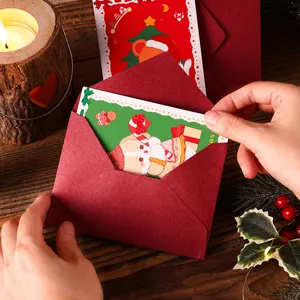 Gros plan d'une main insérant une carte de Noël cartoon dans une enveloppe rouge