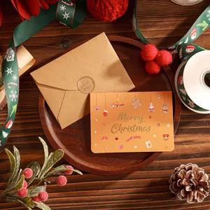 Carte de vœux de Noël festive avec lettrage doré et enveloppe kraft sur plateau.