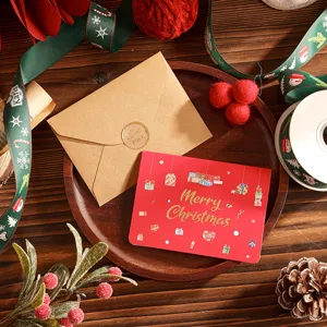 Carte de vœux de Noël rouge avec lettrage doré et enveloppe kraft sur fond de bois
