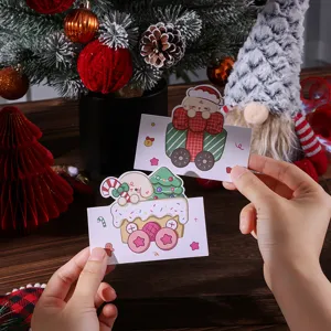 Mains tenant deux cartes de Noël colorées en dessin animé dans un décor festif