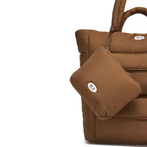 Detailopname van de zachte gewatteerde textuur van een bruine puffer tote tas met bijpassend etui