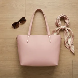 Bolso de mano rosa grande para mujer con gafas de sol sobre suelo de madera clara